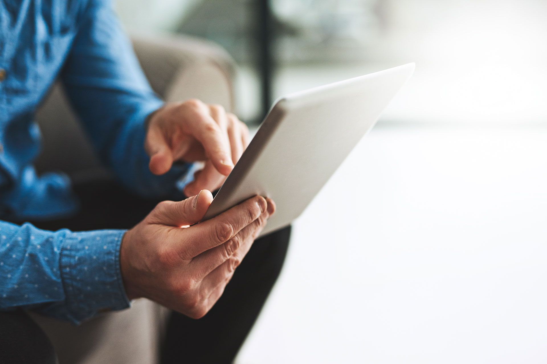 Mann in blauem Hemd bedient Tablet mit beiden Händen – moderne digitale Steuerung oder Informationsnutzung.